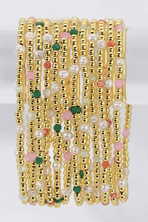 A stack of multiple gold beaded bracelets with white faux pearls and small pink, green, and peach accent beads, displayed on a clear stand against a white background.