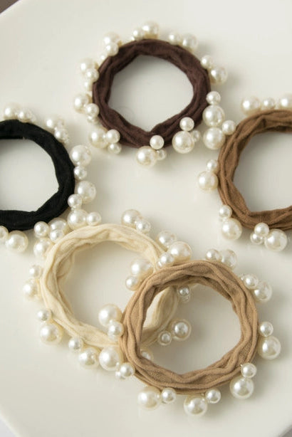 Set of five pearl-adorned hair ties in black, brown, beige, and white on a white surface.